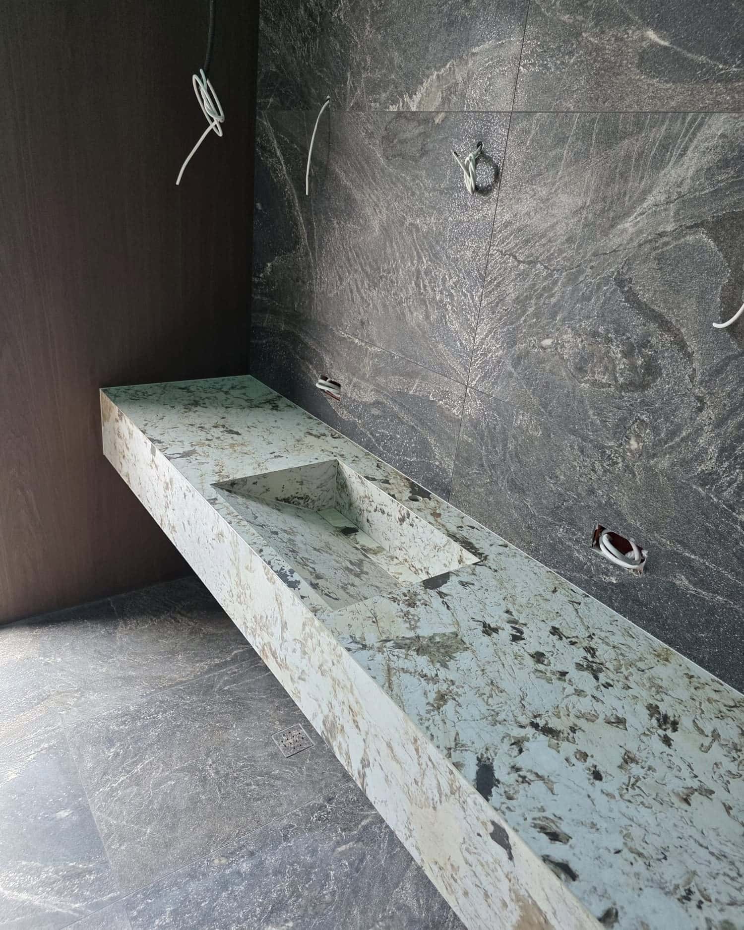 Blat-lavoar lung placat cu piatră verde-deschis, pe perete cu aspect de piatră închisă