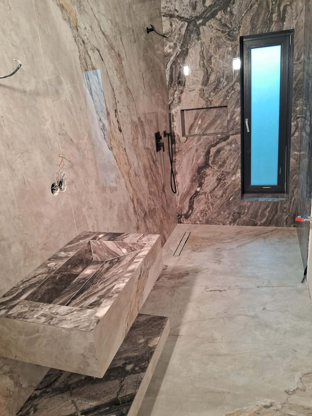 Baie cu lavoar placat cu aspect de marmură închisă cu vinișoare, duș cu baterie neagră și nișă