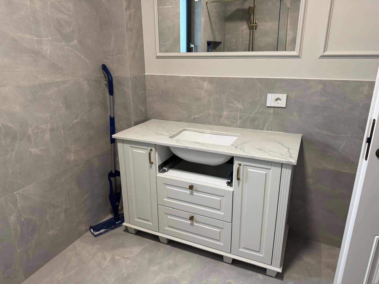 Baie cu plăci gri cu aspect de marmură și mobilier clasic alb, cu blat cu aspect de marmură