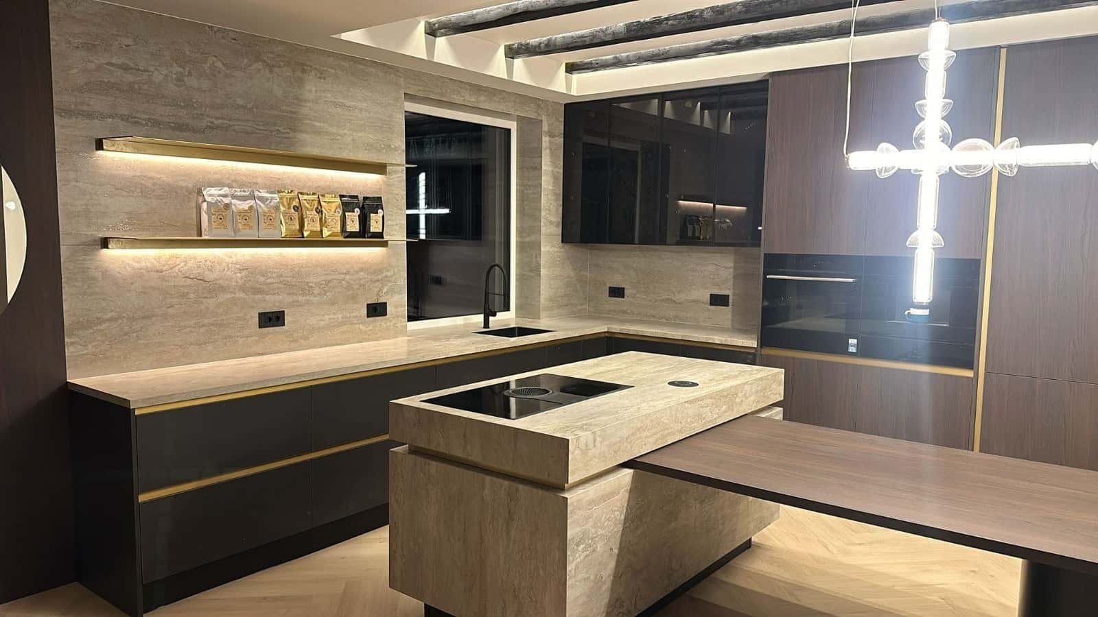 Bucătărie cu insulă și perete cu aspect de travertin, mobilier din lemn închis și iluminat ambiental